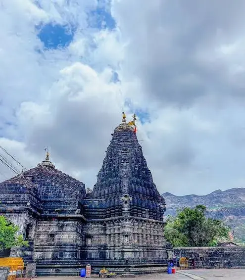 Dark stone Trimbakeshwar temple complex with shikhara and hills beyond the courtyard