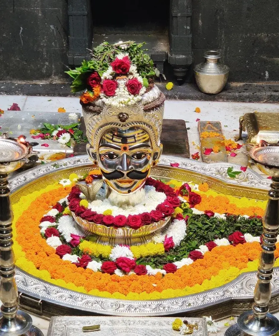 गुलाब, गेंदा और मंदिर दीयों से सुसज्जित रजत मुखलिंग
